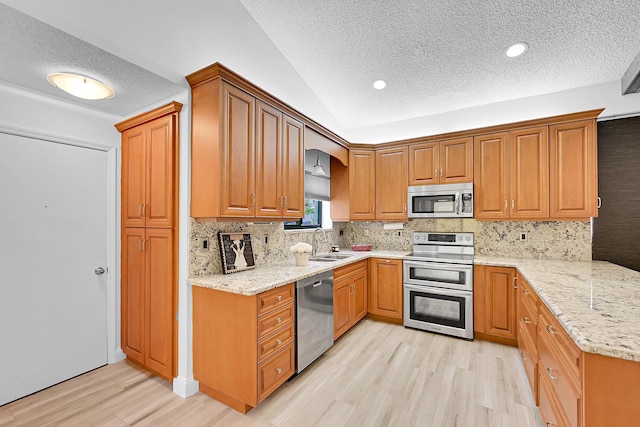 kitchen featuring light stone countertops, appliances with stainless steel finishes, light hardwood / wood-style floors, and sink