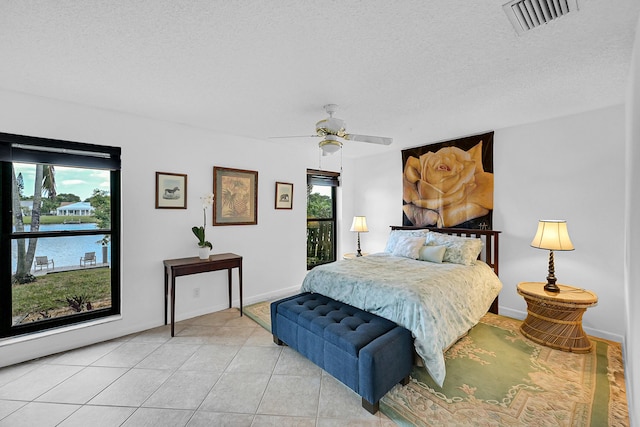 tiled bedroom featuring ceiling fan, multiple windows, and a textured ceiling