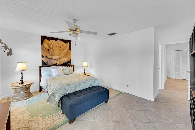 bedroom with a textured ceiling, light tile patterned flooring, visible vents, and a ceiling fan