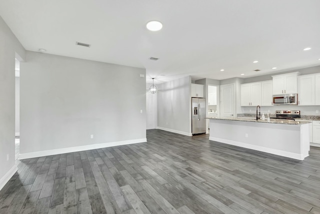 kitchen featuring appliances with stainless steel finishes, hardwood / wood-style floors, white cabinetry, a kitchen island with sink, and light stone counters