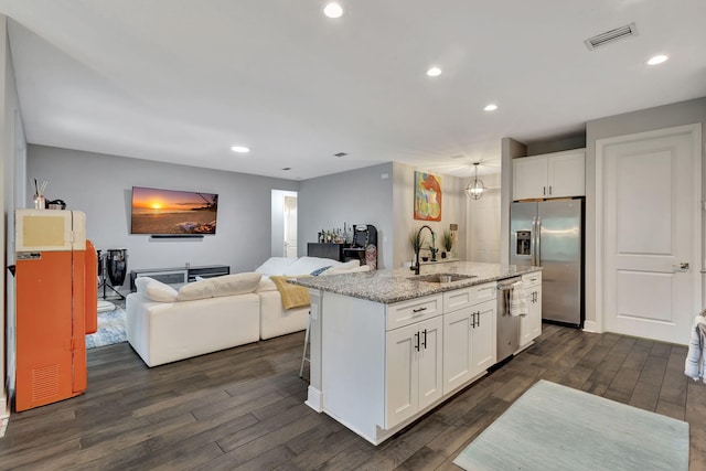 kitchen featuring white cabinets, light stone counters, an island with sink, stainless steel appliances, and sink