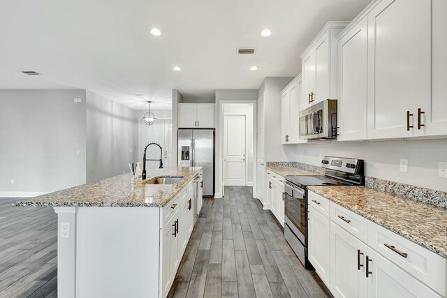 kitchen featuring sink, appliances with stainless steel finishes, white cabinetry, light stone countertops, and a center island with sink