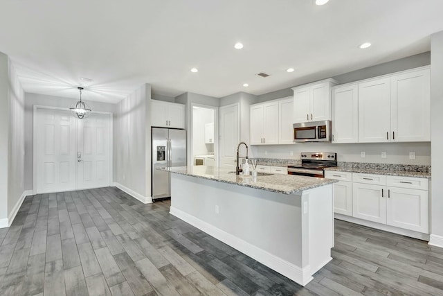 kitchen featuring appliances with stainless steel finishes, decorative light fixtures, sink, white cabinets, and a kitchen island with sink