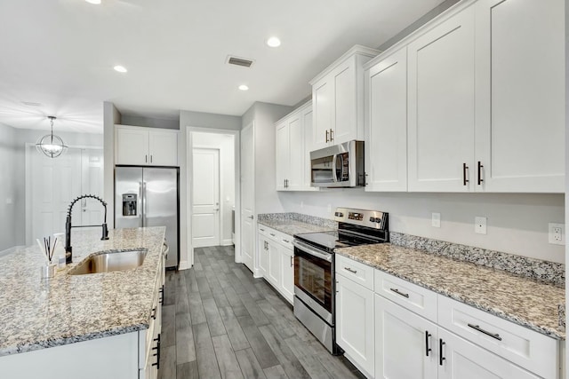 kitchen with sink, white cabinetry, stainless steel appliances, wood-type flooring, and an island with sink