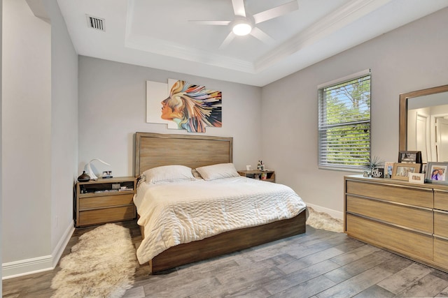 bedroom featuring crown molding, hardwood / wood-style floors, ceiling fan, and a tray ceiling