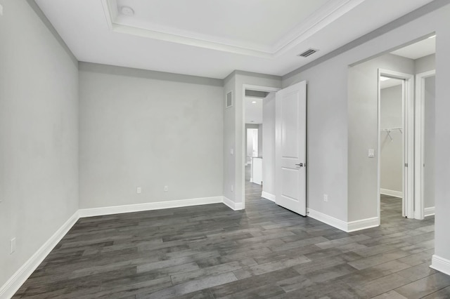 unfurnished bedroom with a spacious closet, dark wood-type flooring, ornamental molding, and a raised ceiling