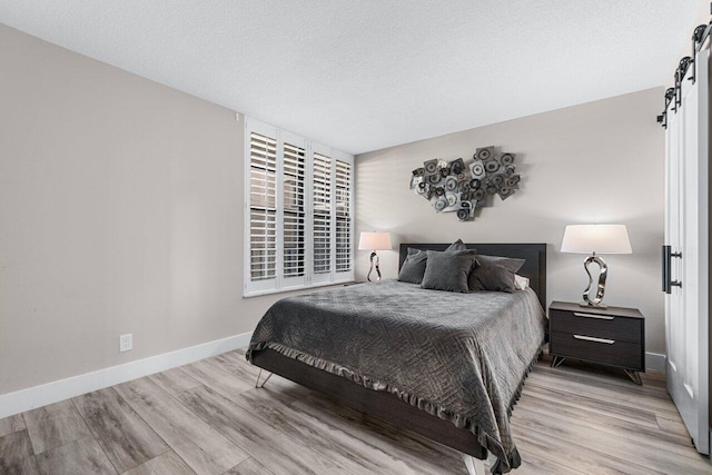 bedroom with a barn door, light hardwood / wood-style floors, and a textured ceiling