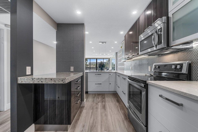 kitchen with dark brown cabinetry, white cabinets, light stone countertops, appliances with stainless steel finishes, and light wood-type flooring