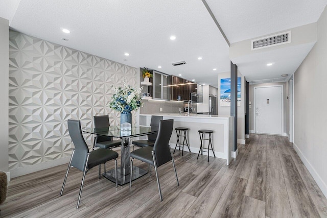 dining area with light wood-type flooring, sink, tile walls, and a textured ceiling