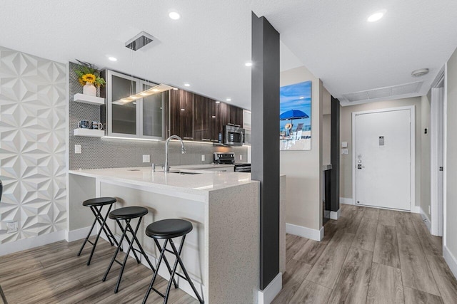 kitchen featuring a breakfast bar area, light hardwood / wood-style flooring, dark brown cabinets, sink, and appliances with stainless steel finishes