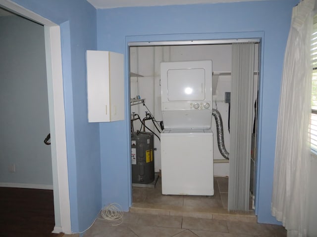 clothes washing area featuring water heater, tile patterned floors, and stacked washing maching and dryer