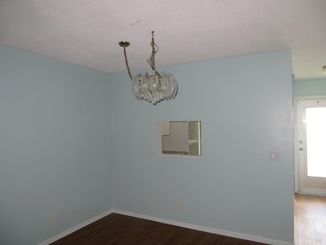 empty room with dark wood-type flooring and an inviting chandelier