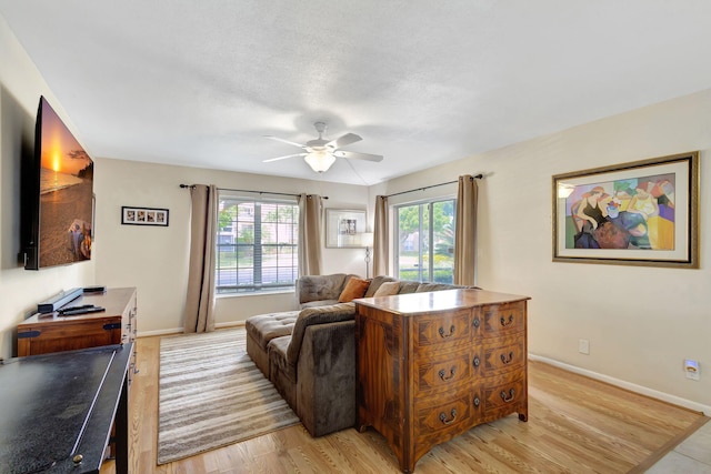 living room with light hardwood / wood-style flooring, a textured ceiling, and ceiling fan