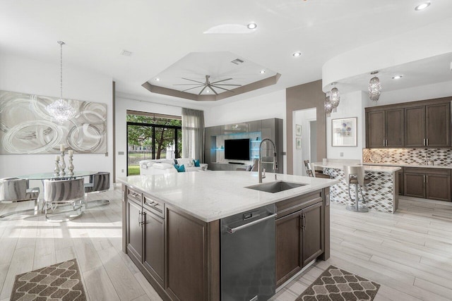 kitchen featuring decorative backsplash, light hardwood / wood-style flooring, an island with sink, a tray ceiling, and sink