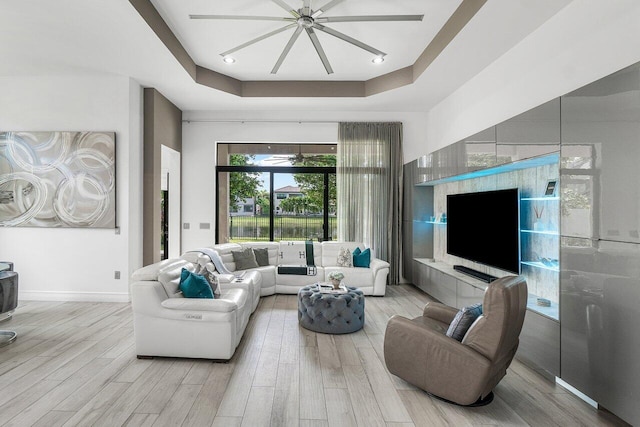 living room with ceiling fan, light wood-type flooring, and a raised ceiling