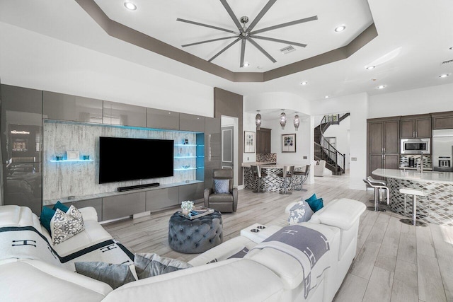 living room with ceiling fan, a tray ceiling, and light hardwood / wood-style flooring