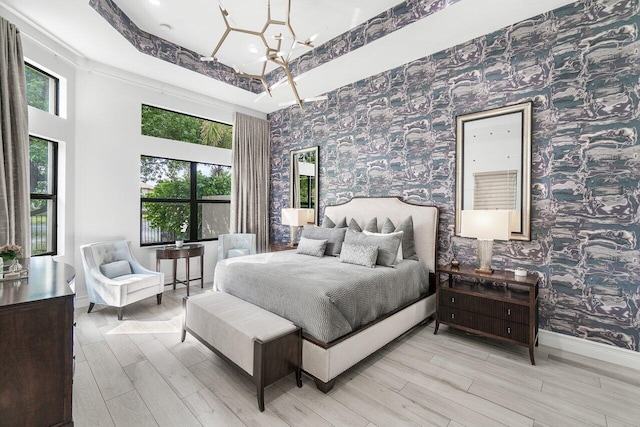 bedroom with a tray ceiling, a towering ceiling, light hardwood / wood-style flooring, and an inviting chandelier