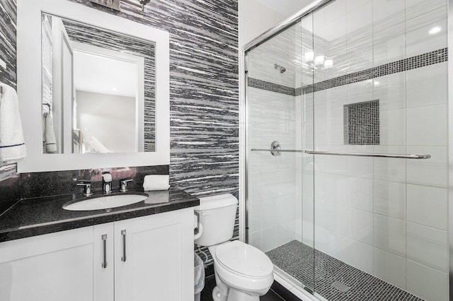 bathroom featuring toilet, a shower with shower door, vanity, and tile walls