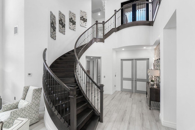 staircase featuring french doors, hardwood / wood-style floors, and a high ceiling