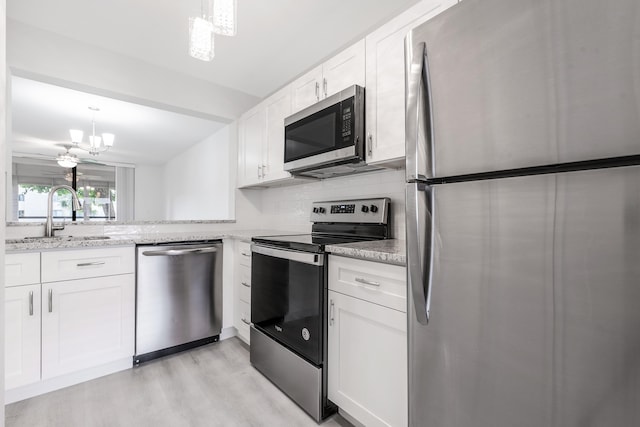 kitchen with appliances with stainless steel finishes, light stone counters, light hardwood / wood-style floors, and white cabinets