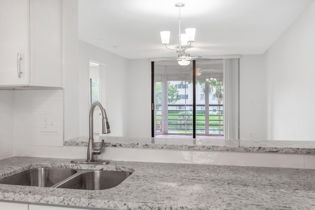 kitchen featuring pendant lighting, light stone countertops, sink, and white cabinetry