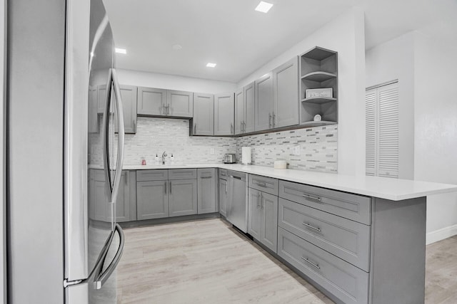 kitchen with appliances with stainless steel finishes, kitchen peninsula, light hardwood / wood-style flooring, and gray cabinetry