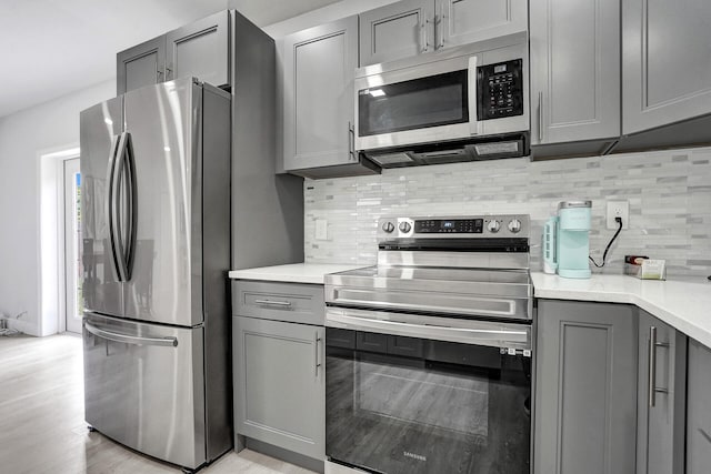 kitchen featuring tasteful backsplash, appliances with stainless steel finishes, light wood-type flooring, and gray cabinets