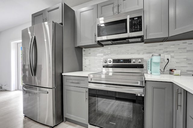 kitchen with backsplash, stainless steel appliances, light hardwood / wood-style floors, and gray cabinetry