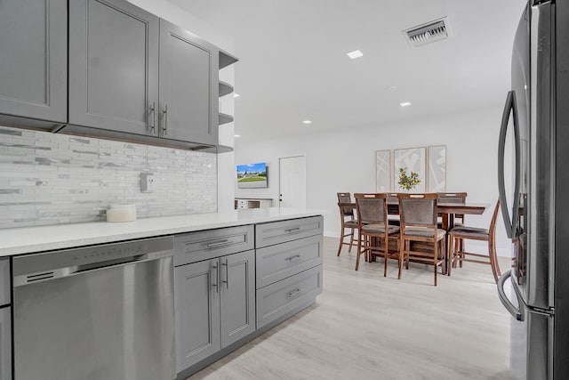 kitchen with appliances with stainless steel finishes, light hardwood / wood-style flooring, tasteful backsplash, and gray cabinets