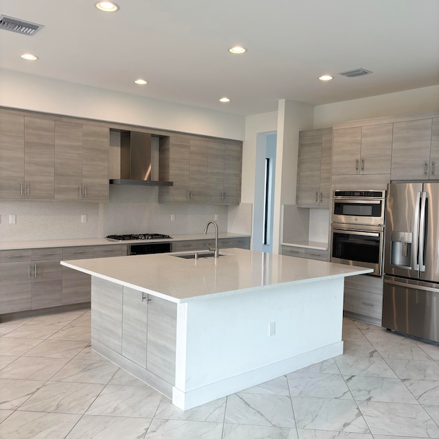 kitchen with wall chimney exhaust hood, appliances with stainless steel finishes, sink, and an island with sink