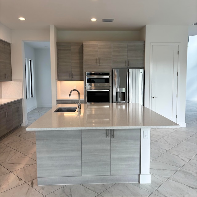 kitchen featuring an island with sink, appliances with stainless steel finishes, a kitchen breakfast bar, light stone countertops, and sink