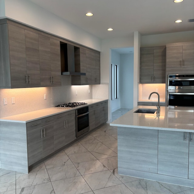 kitchen featuring wall chimney range hood, sink, light stone countertops, gray cabinets, and appliances with stainless steel finishes