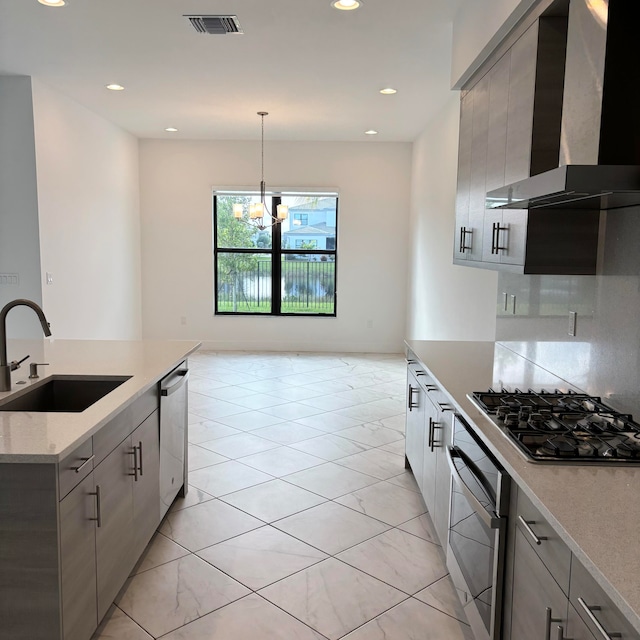 kitchen featuring wall chimney exhaust hood, sink, pendant lighting, a chandelier, and appliances with stainless steel finishes