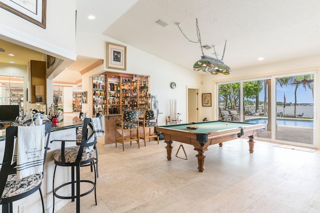 rec room featuring vaulted ceiling, a water view, a textured ceiling, and bar area