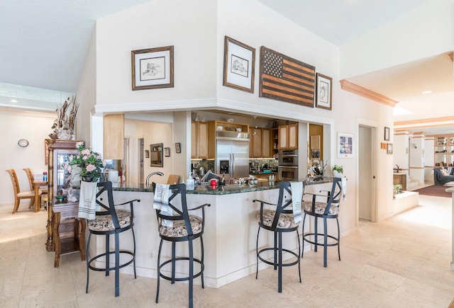 kitchen featuring a kitchen bar, kitchen peninsula, dark stone countertops, and appliances with stainless steel finishes