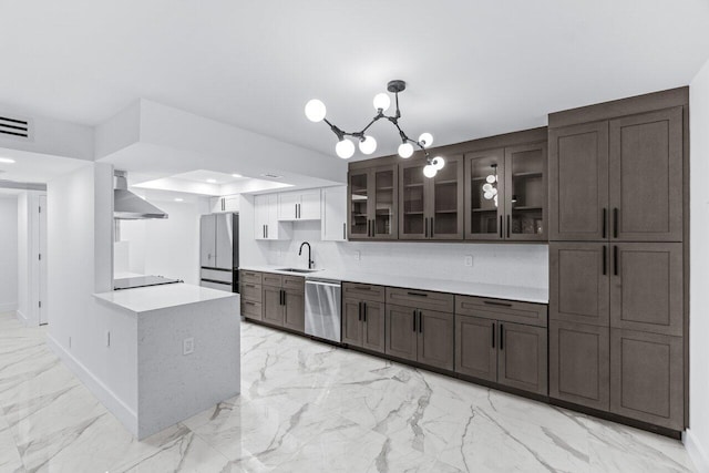 kitchen with wall chimney range hood, appliances with stainless steel finishes, sink, hanging light fixtures, and a chandelier