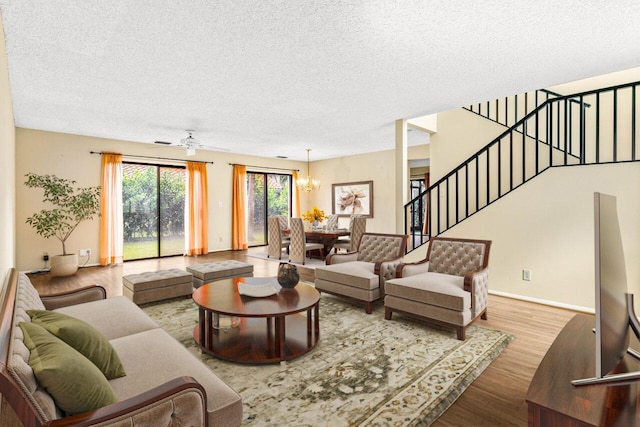 living room featuring wood-type flooring, ceiling fan with notable chandelier, and a textured ceiling