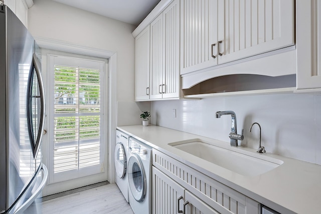 laundry area featuring separate washer and dryer, sink, light hardwood / wood-style flooring, and cabinets