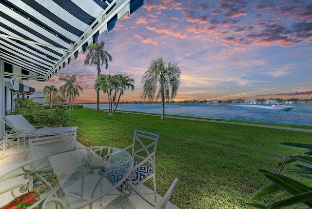 yard at dusk featuring a water view and a lawn