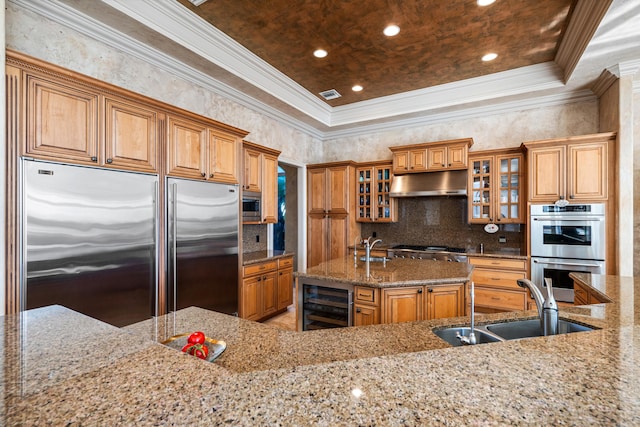 kitchen featuring light stone countertops, sink, an island with sink, beverage cooler, and built in appliances