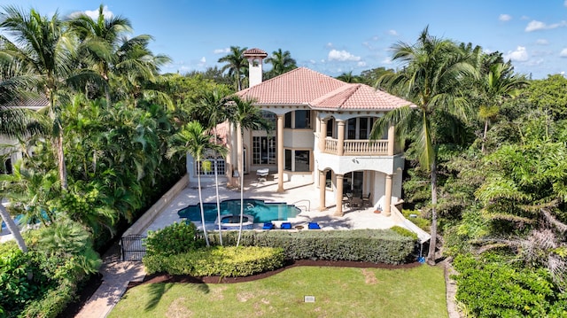 back of house featuring a balcony, a swimming pool with hot tub, a patio, and a lawn