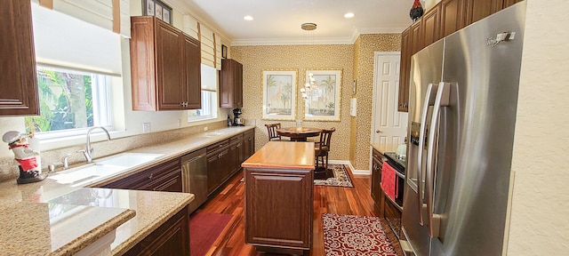 kitchen with sink, ornamental molding, appliances with stainless steel finishes, a kitchen island, and dark hardwood / wood-style flooring