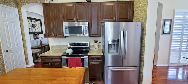 kitchen featuring dark brown cabinets, dark hardwood / wood-style flooring, light stone counters, and appliances with stainless steel finishes