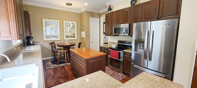 kitchen with a center island, dark wood-type flooring, light stone counters, crown molding, and appliances with stainless steel finishes