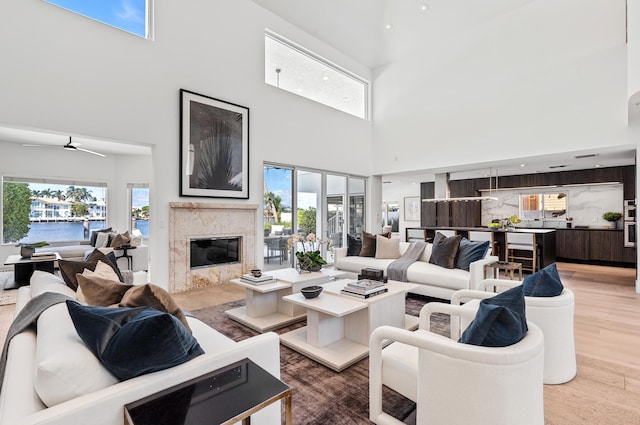 living room featuring a high ceiling, wood-type flooring, a high end fireplace, a water view, and ceiling fan