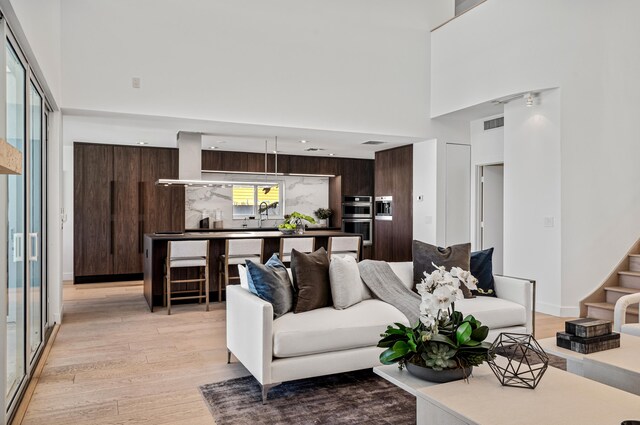 living room featuring sink, light hardwood / wood-style floors, and a towering ceiling