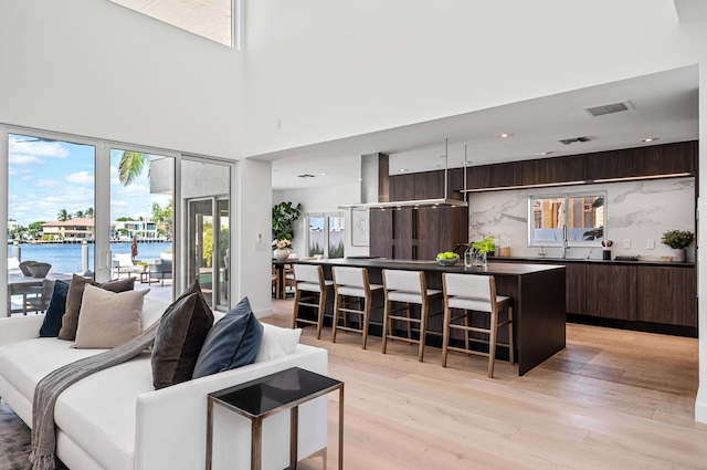 living room featuring light hardwood / wood-style flooring, a high ceiling, sink, and a water view