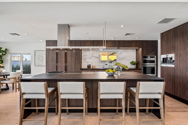 kitchen featuring light hardwood / wood-style floors, dark brown cabinets, a kitchen island, and stainless steel double oven