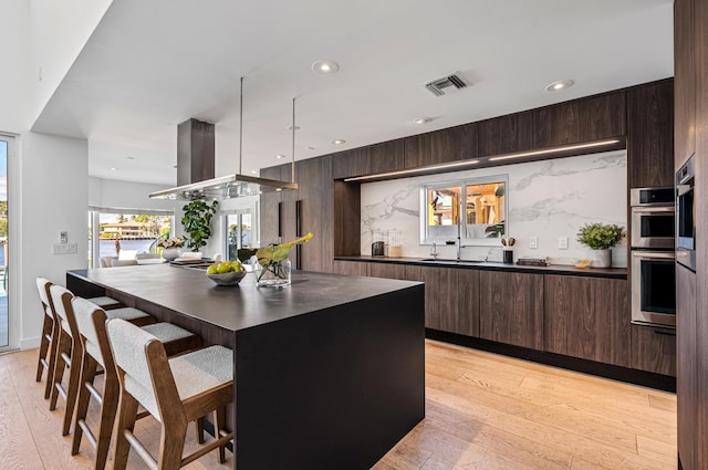 kitchen featuring light hardwood / wood-style flooring, double oven, a center island, and a breakfast bar area