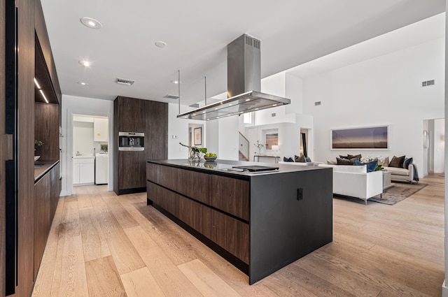 kitchen featuring island exhaust hood, an island with sink, dark brown cabinets, and light wood-type flooring